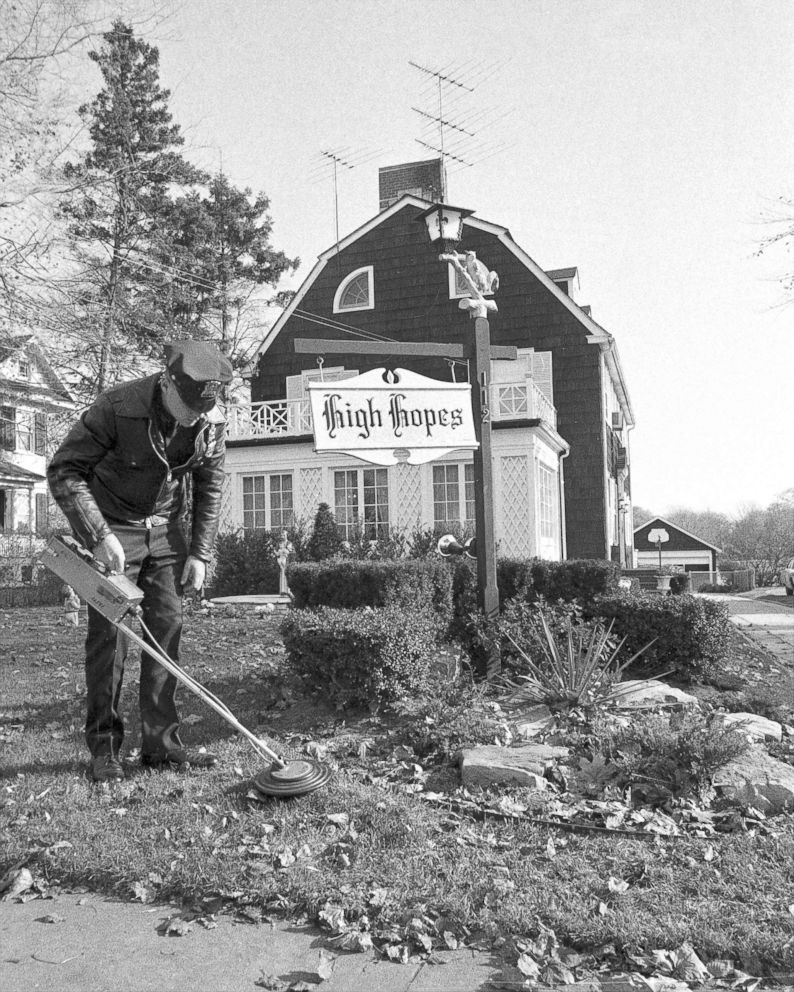 PHOTO: Suffolk County policeman uses mine detector as he sweeps through dead leaves on lawn of Ronald DeFeo's 12-room, $75,000 Dutch colonial home in Amityville.