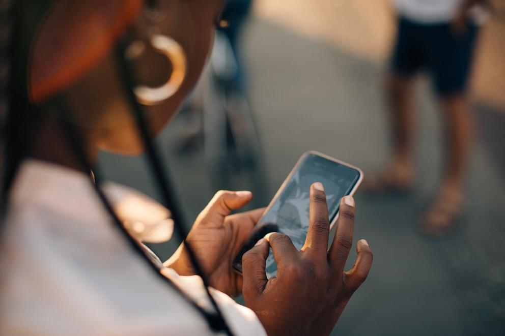 PHOTO: Cropped image of young woman using smart phone while standing on street in city.