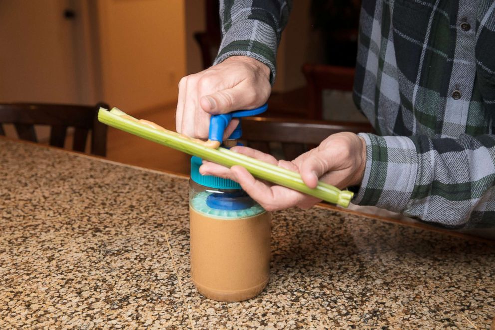 PHOTO: The Peanut Butter Pump tube nozzle dispenses peanut butter onto a stick of celery. 