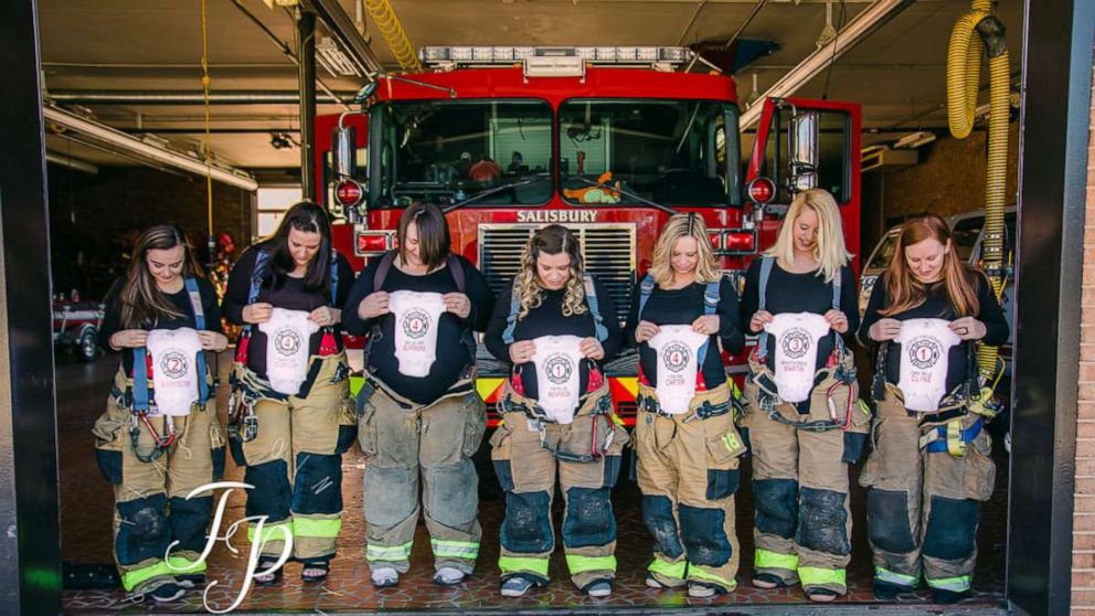 Seven women who are all pregnant and married to Salisbury, North Carolina, firefighters pose in front of the station.