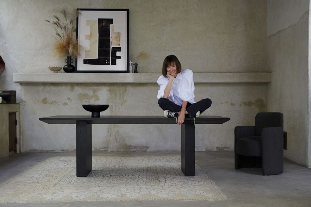 PHOTO: Leanne Ford sitting on a dining table from her collection with Crate and Barrel.