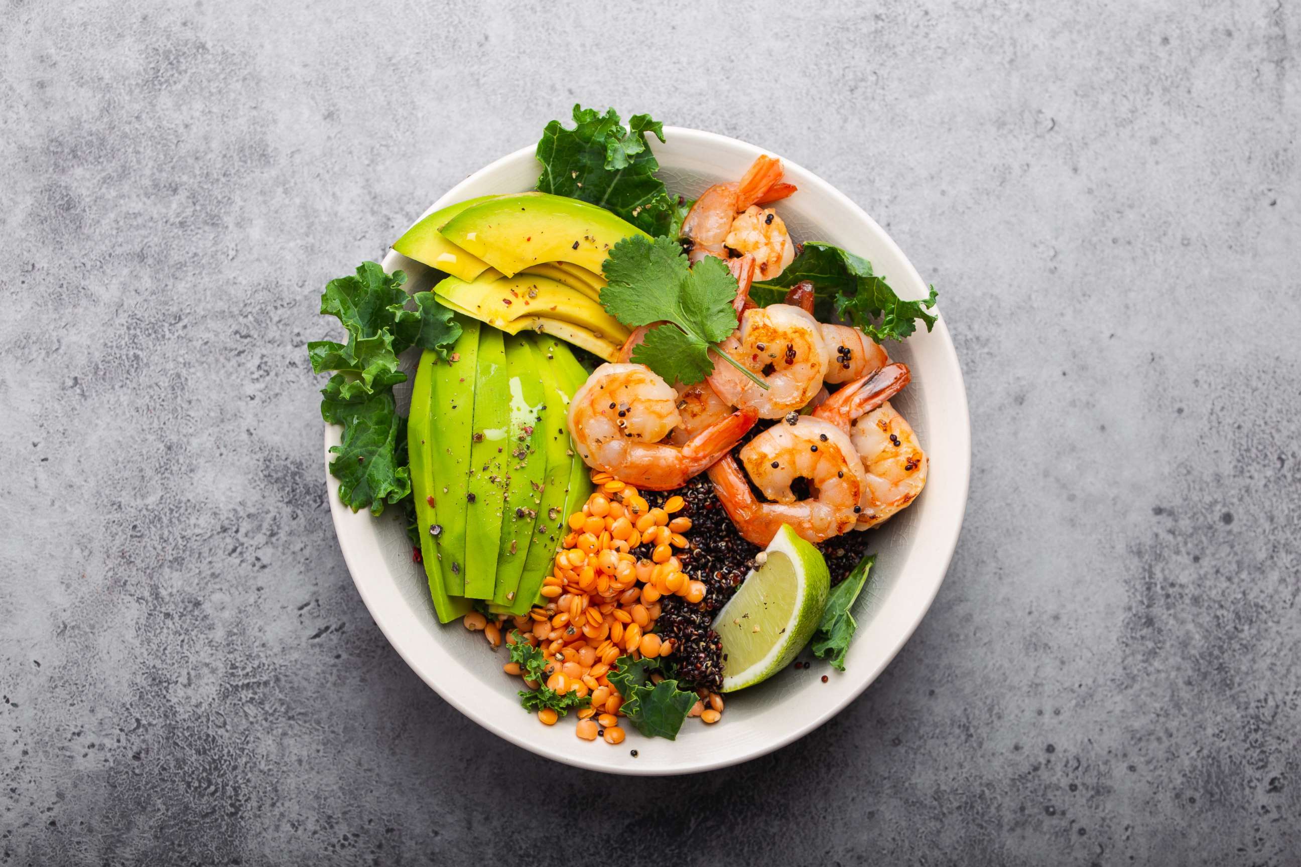 PHOTO: Top view of salad bowl with shrimp, avocado, fresh kale, quinoa, red lentils, lime and olive oil.