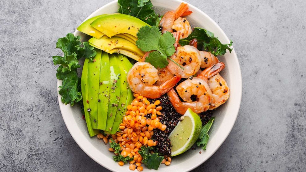 Top view of salad bowl with shrimp, avocado, fresh kale, quinoa, red lentils, lime and olive oil.