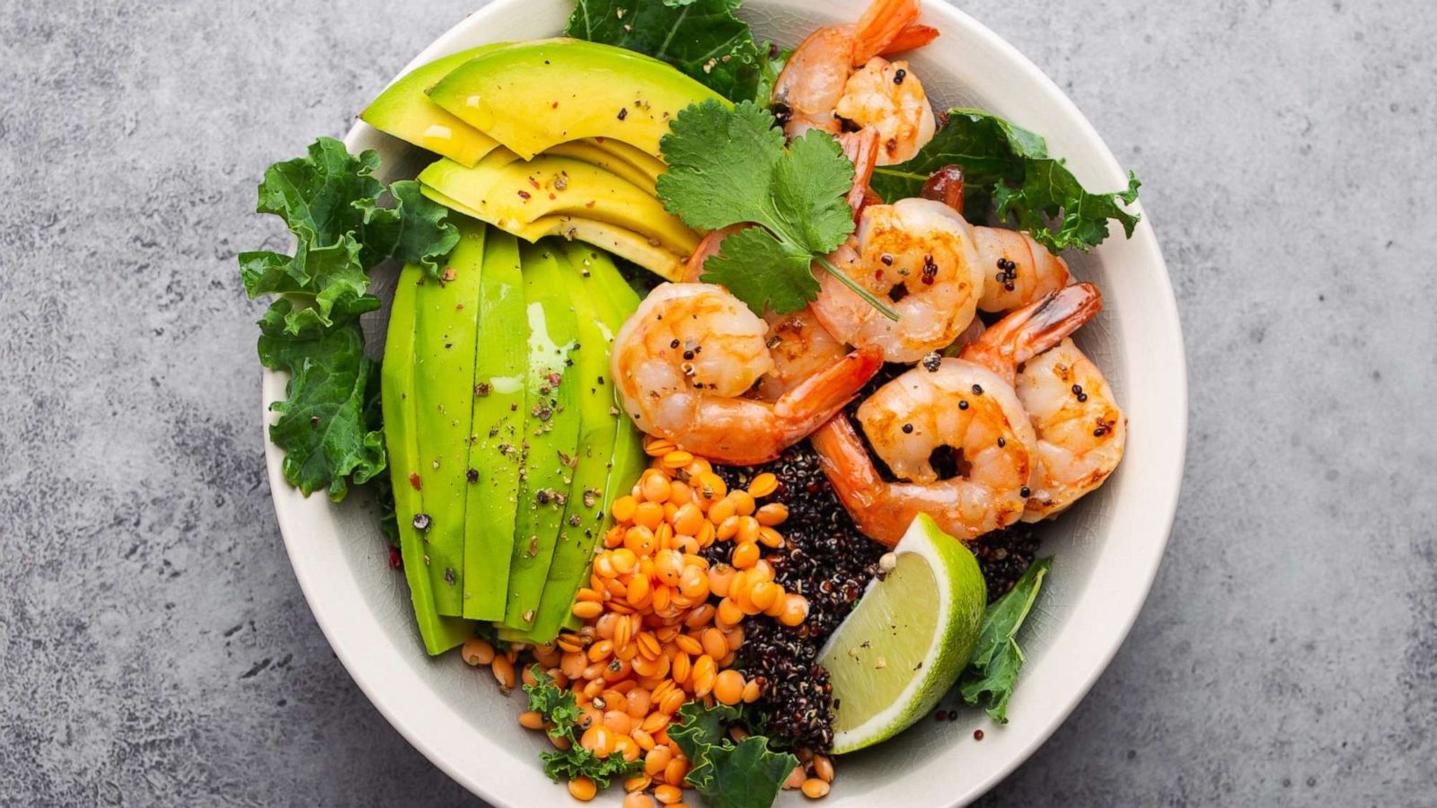 PHOTO: Top view of salad bowl with shrimp, avocado, fresh kale, quinoa, red lentils, lime and olive oil.