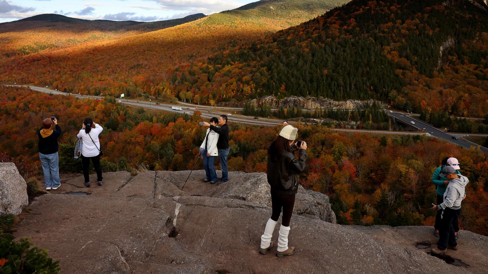 PHOTO: People take photos of the fall foliage as they look out from the top of Artist's Bluff in Franconia Notch State Park, N.H., Oct. 8, 2024.