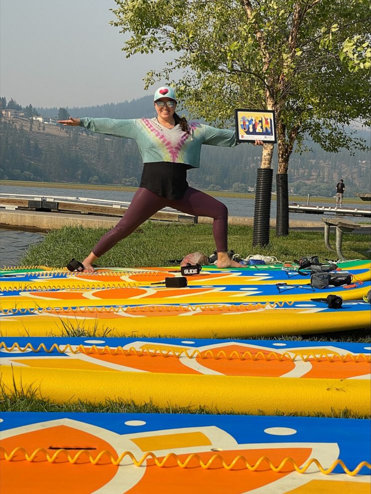 PHOTO:  Roxanne Best poses in a yoga position holding the 'Open for Business' Sign Yeshi created for her to represent strength and resilience amid the COVID-19 pandemic.