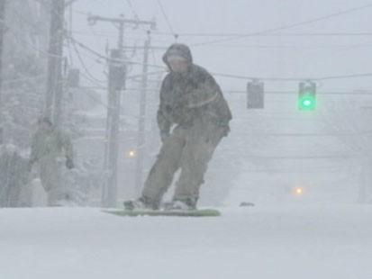 VIDEO: Someone snowboarding down a street.