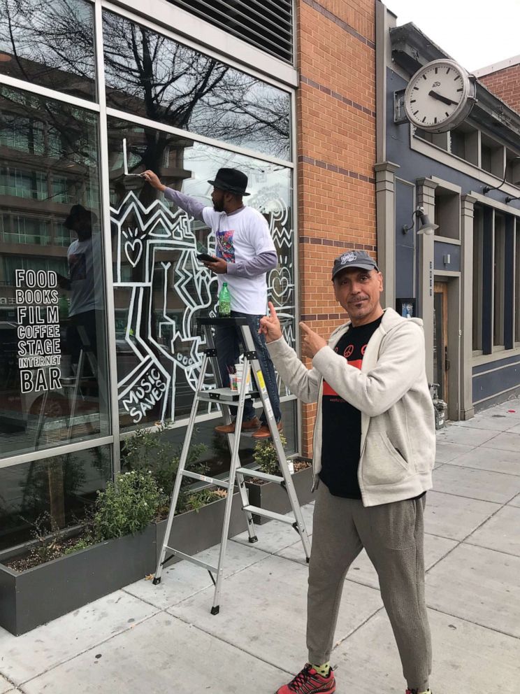 PHOTO: Owner Andy Shallal joins artist James Terrell as he paints the store front of the Busboys and Poets 14th Street location in Washington. D.C.