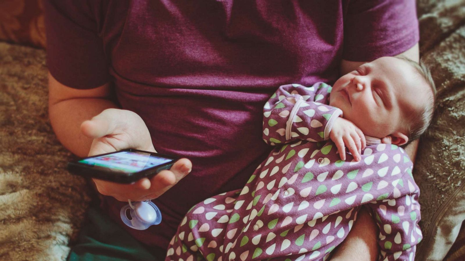 PHOTO: Stock photo of father using a cellphone while holding his newborn baby.