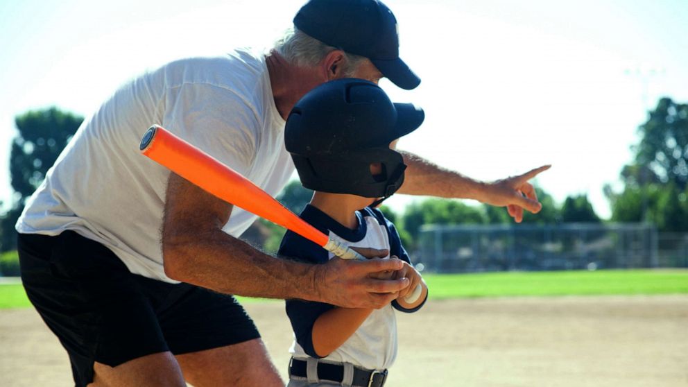 PHOTO: An older man helps coach a child with batting skills in this stock photo.