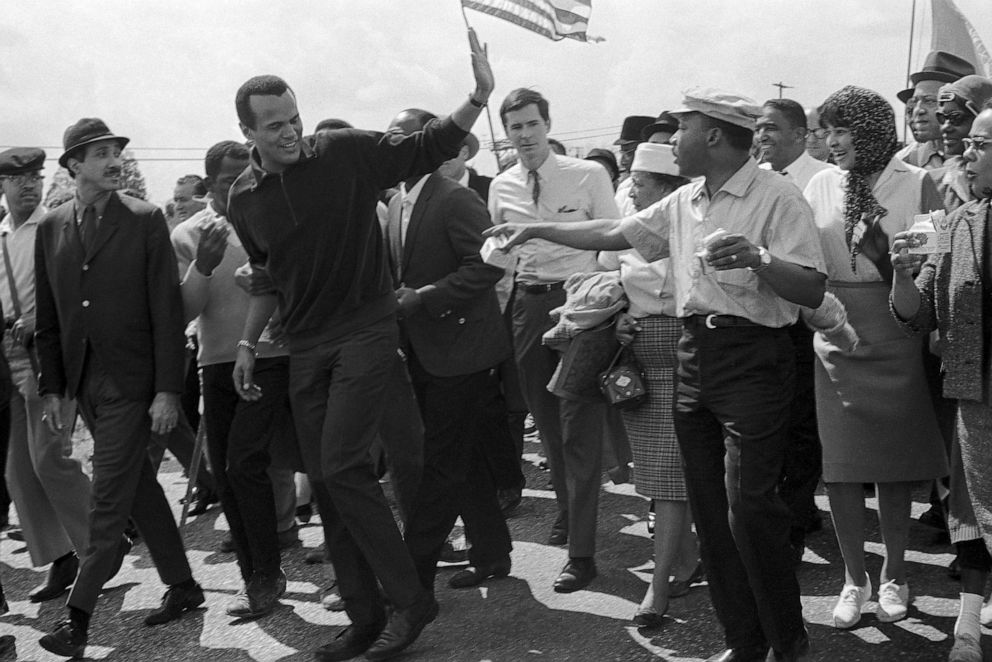 PHOTO: Singer Harry Belafonte waves to Dr.  Martin Luther King, Jr., right, as he exits the column of civil rights protesters after walking with them March 24, 1965 in Montgomery, Alabama.