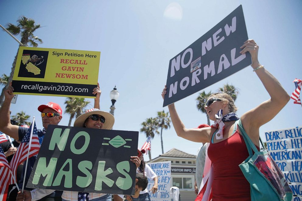 PHOTO: Demonstrators hold signs as they protest the lockdown and wearing masks, June 27, 2020, in Huntington Beach, Calif.
