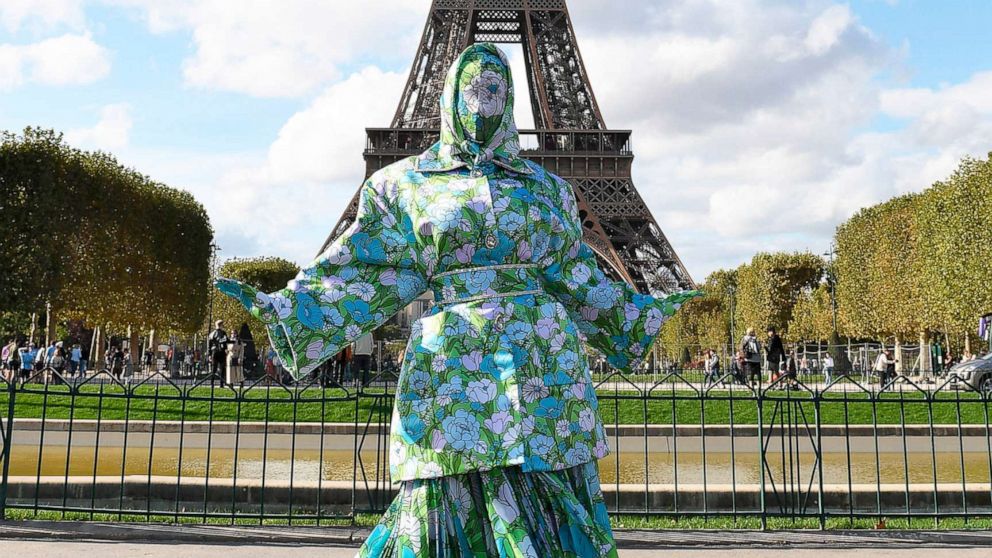 On Instagram, she released a video strolling in front of the Eiffel Tower with a matching green and blue floral-print headscarf, belted blazer, skirt, stockings and her face fully covered.