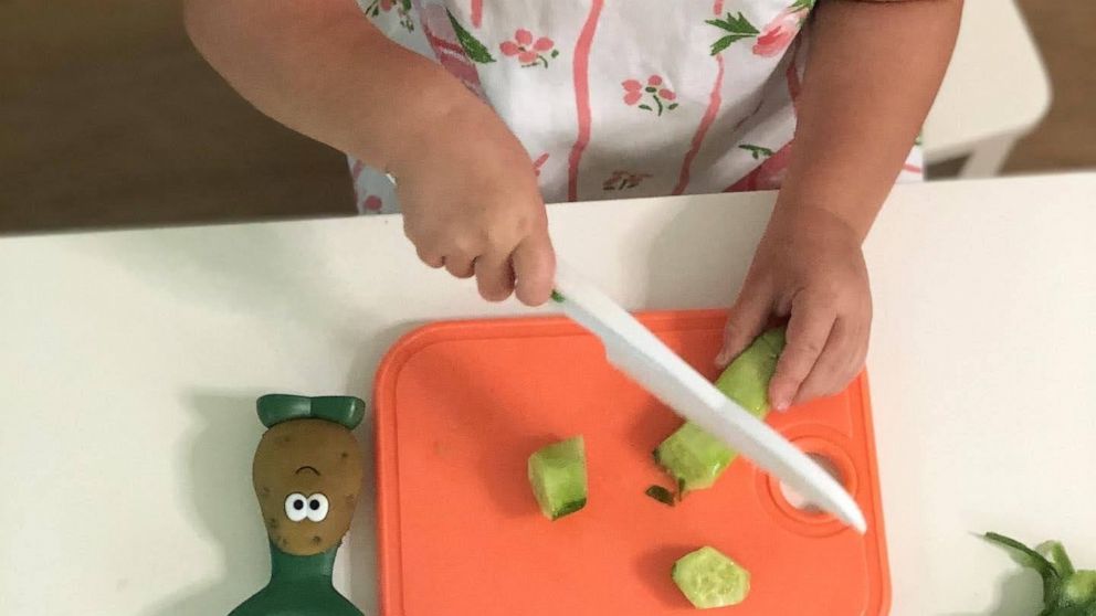Charlotte chops a cucumber with the toddler kitchen knife.