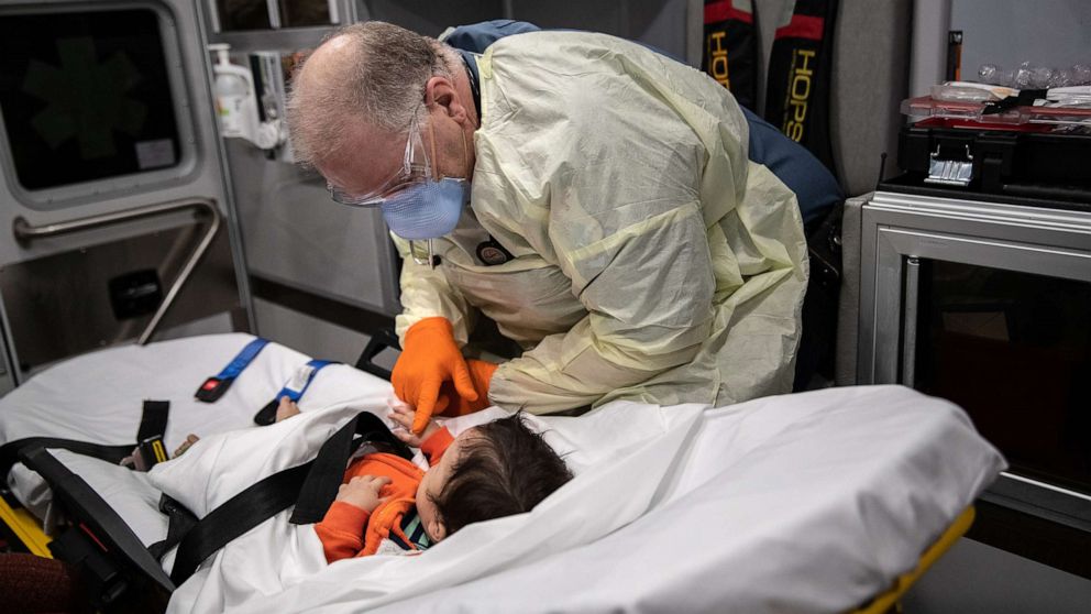 PHOTO: Paramedic Randy Lilly, wearing personal protection equipment (PPE), sits with a 10-month-old boy with fever while riding by ambulance to Stamford Hospital, April 4, 2020, in Stamford, Conn.