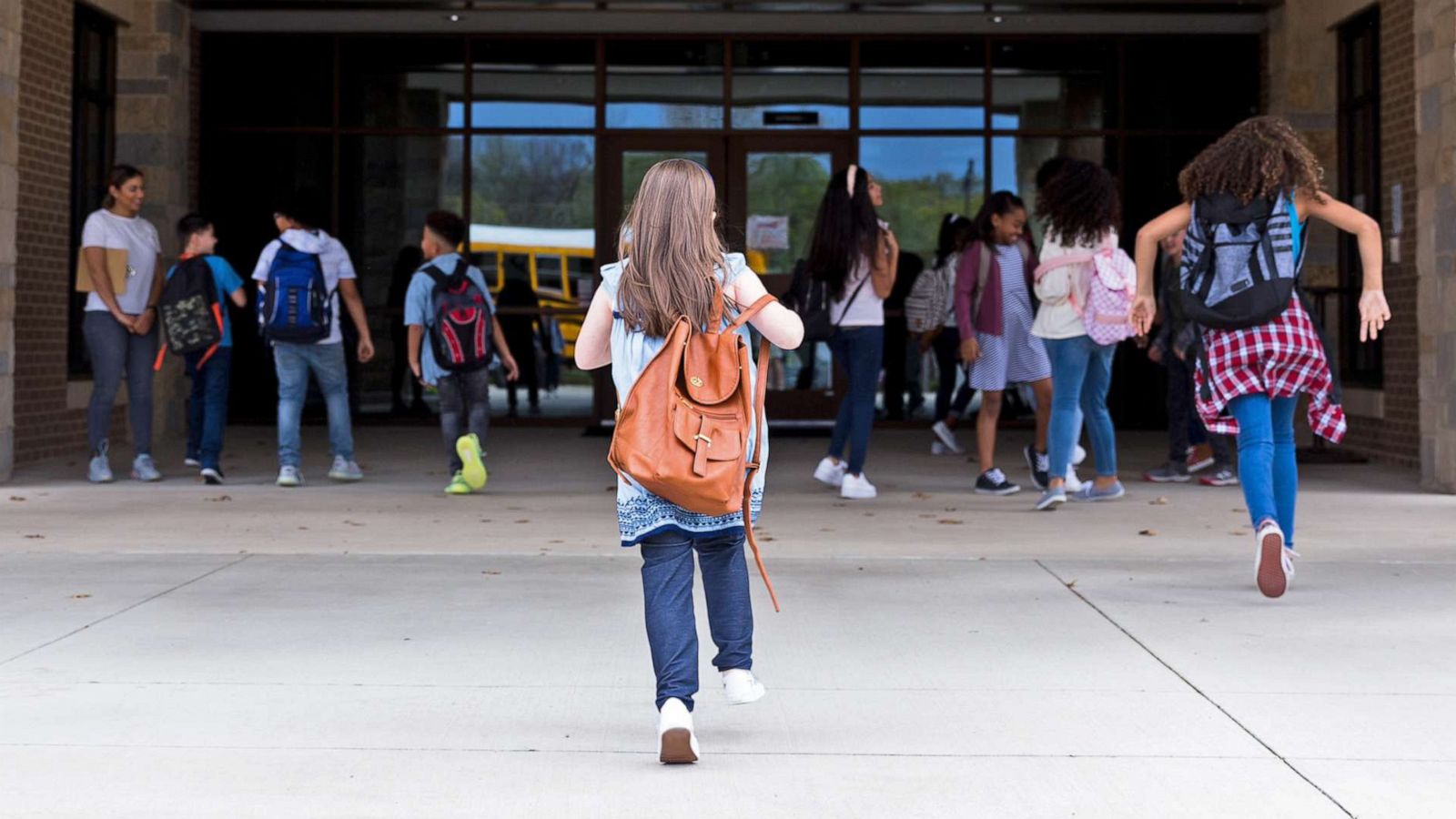 PHOTO: Rear view of elementary schoolgirl walking into the school building