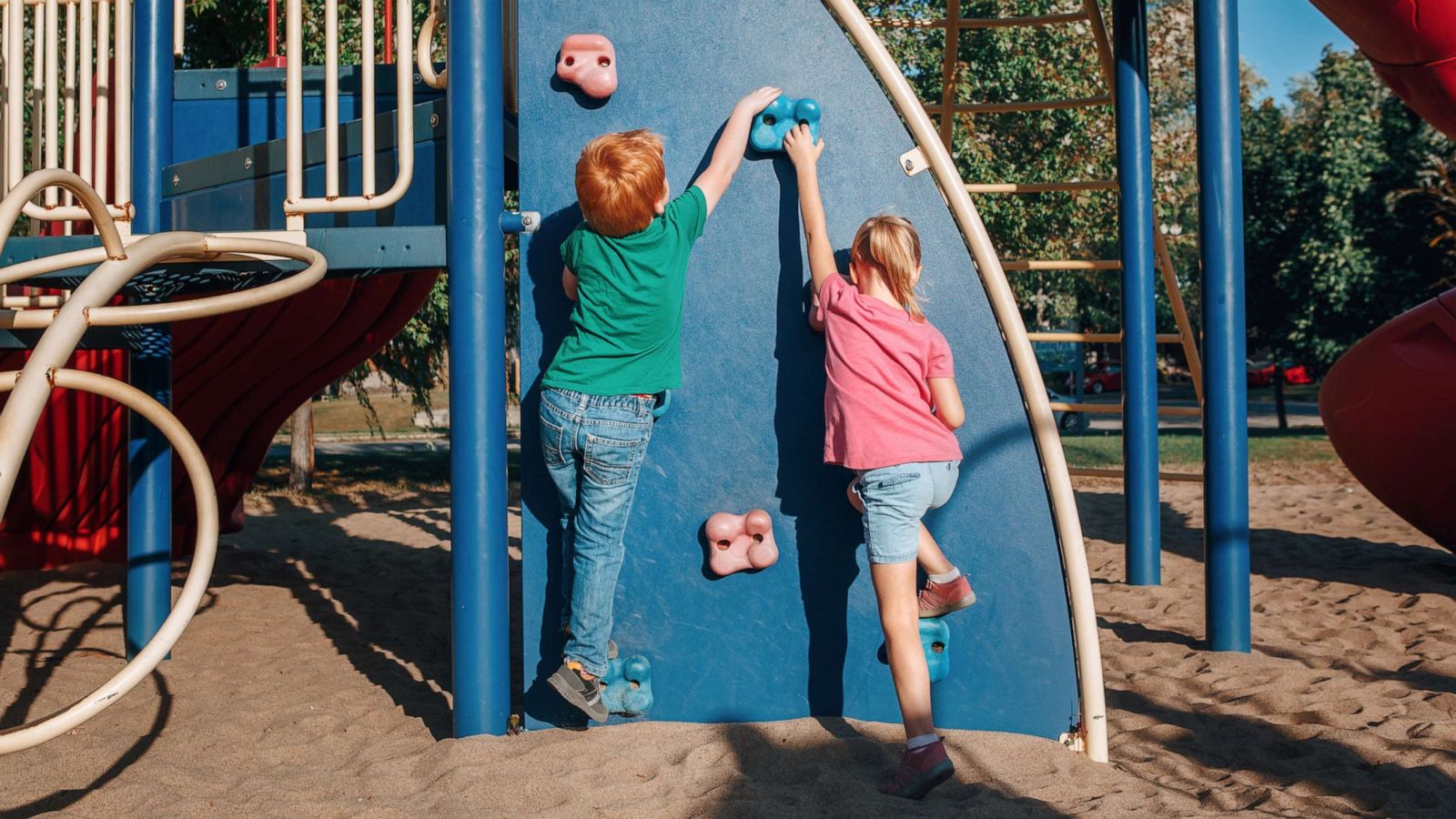 PHOTO: Little preschool boy and girl climbing rock wall at a playground outside on summer day.