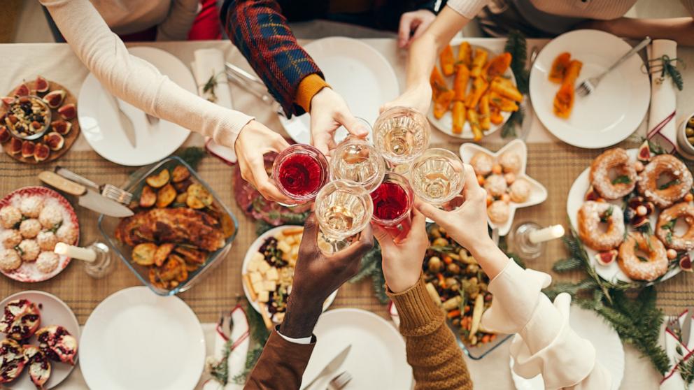 PHOTO: Top view of people raising glasses over festive dinner table while celebrating Christmas with friends and family.