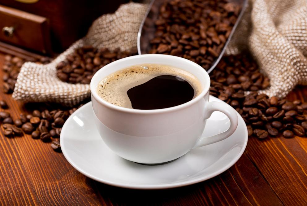 PHOTO: A cup of black coffee is seen next to coffee beans on a wooden table.