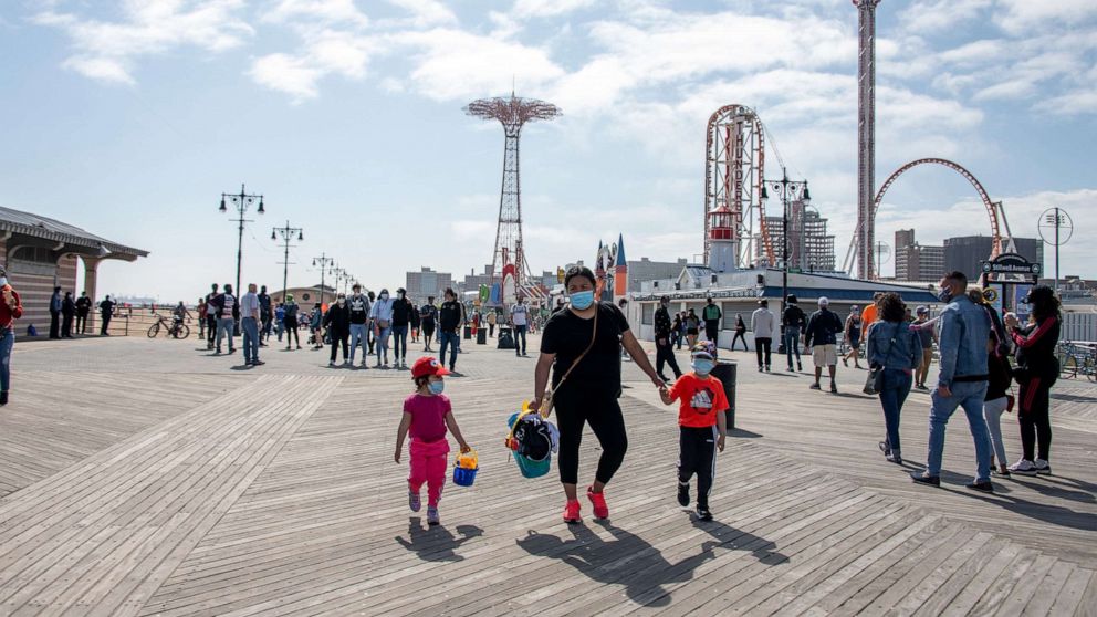 PHOTO: In this May 25, 2020, file photo, people wearing masks walk on the boardwalk at Coney Island with a view of Luna Park in the background in New York.