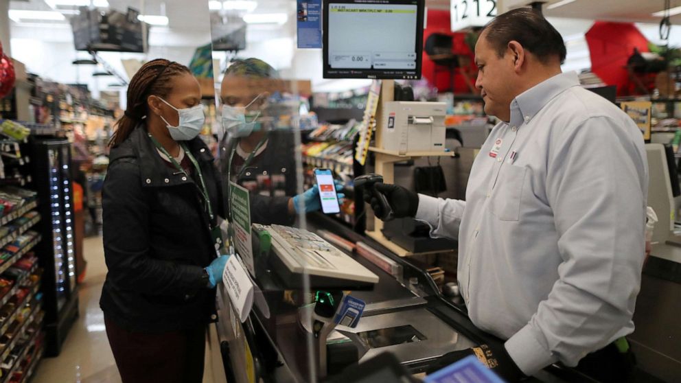 PHOTO: Assistant store manager Jesus Alvarez rings up groceries from behind a new plexiglass barrier at Ralphs Kroger grocery store in Los Angeles, March 30, 2020.