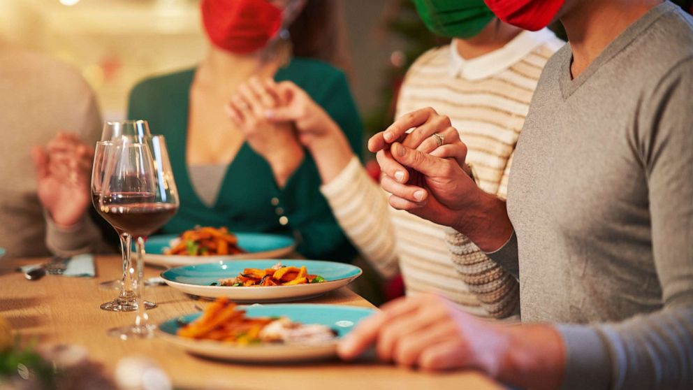 PHOTO: A group of people pray over a holiday table while wearing masks in an undated stock photo.