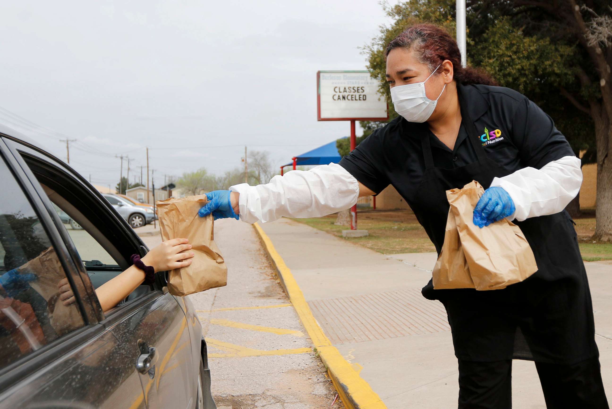 PHOTO: Burleson Elementary School's cafeteria manager Geneva Garcia hands a sack lunch to a family outside a school building in Odessa, Texas, March 17, 2020.
