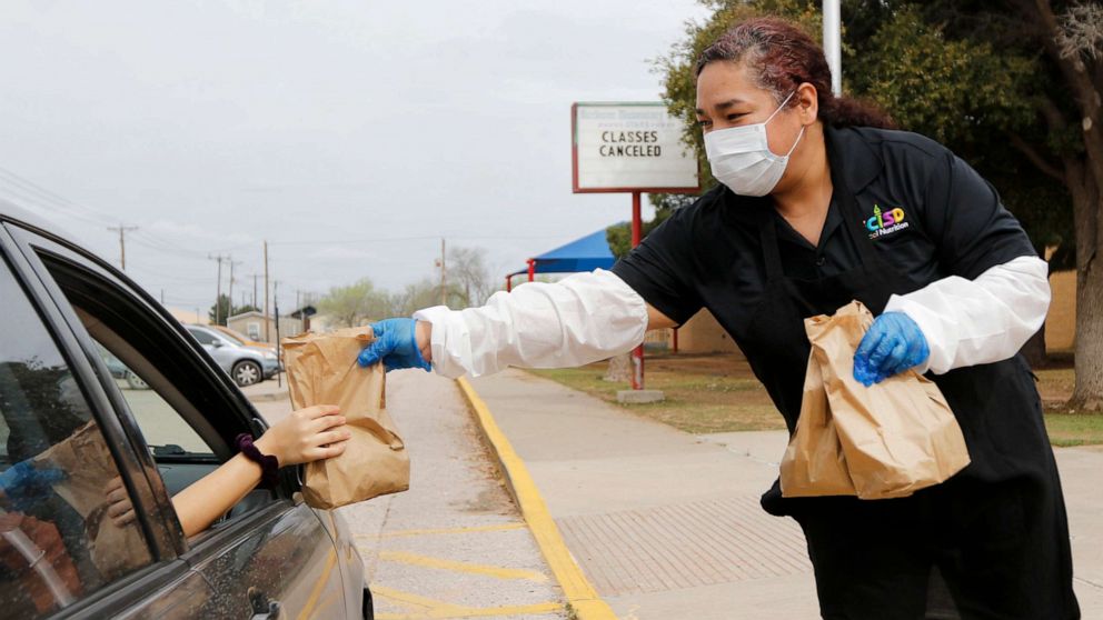 PHOTO: Burleson Elementary School's cafeteria manager Geneva Garcia hands a sack lunch to a family outside a school building in Odessa, Texas, March 17, 2020.
