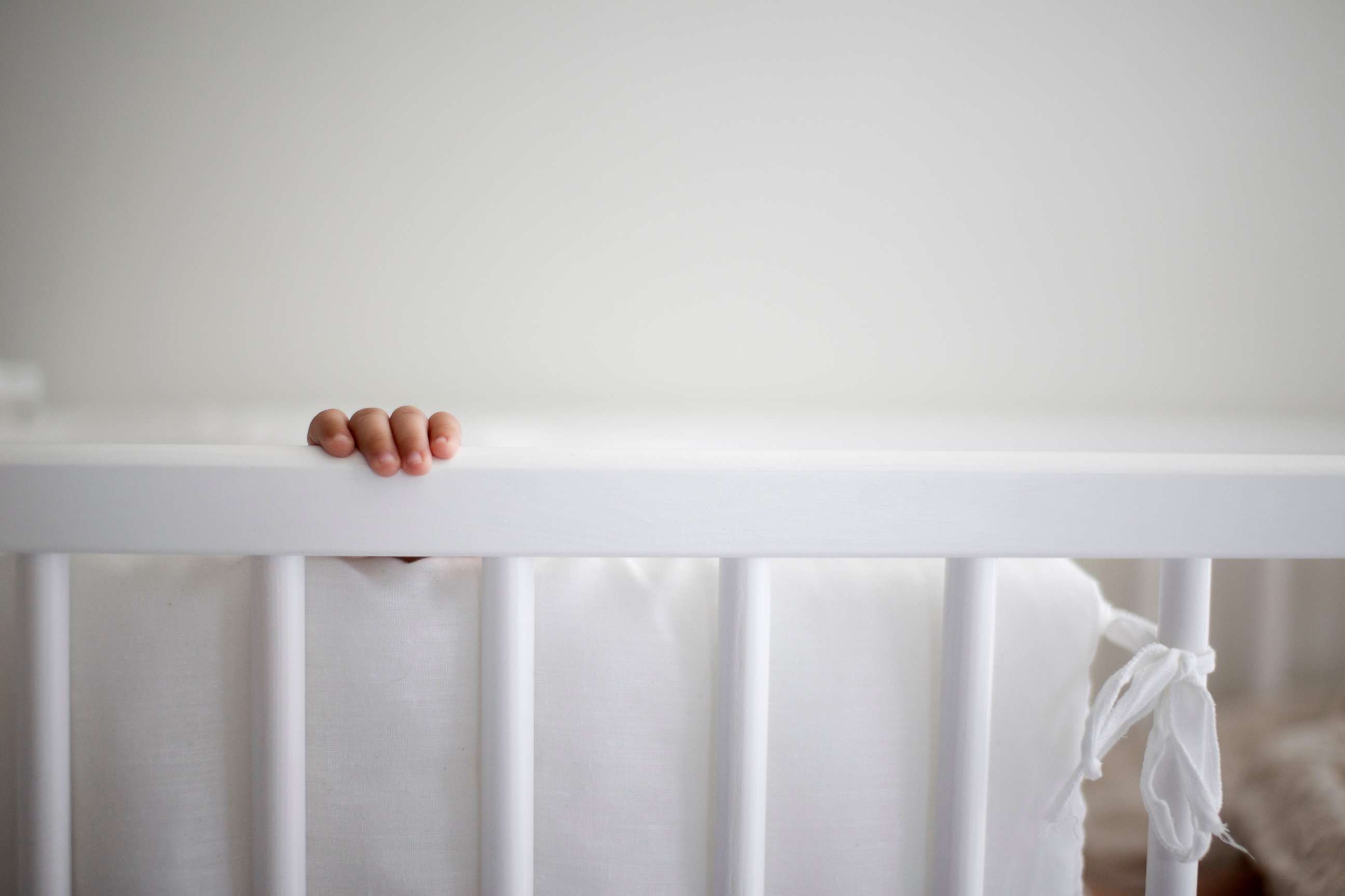 PHOTO: A baby's hand reaches for the rail of a crib that has a bumper tied to the rails.