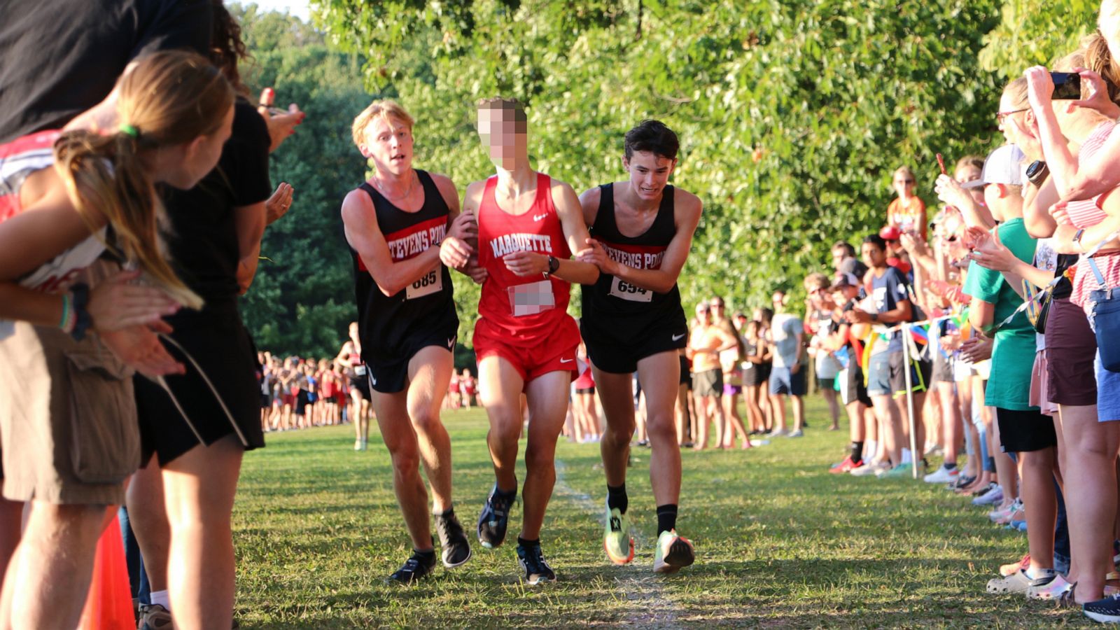 PHOTO: Two cross-country runners from Wisconsin's Stevens Point Area Senior High stop to help a competitor cross the finish line during a meet on Aug. 25, 2023.