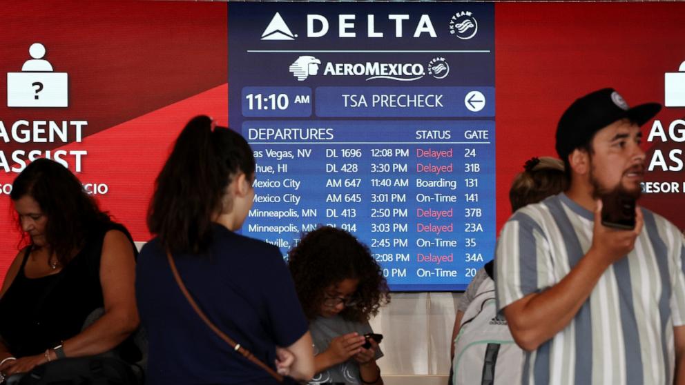 PHOTO: Travelers wait in line, as a flight board shows delays, on the check-in floor of the Delta Air Lines terminal at Los Angeles International Airport (LAX) on July 23, 2024 in Los Angeles.