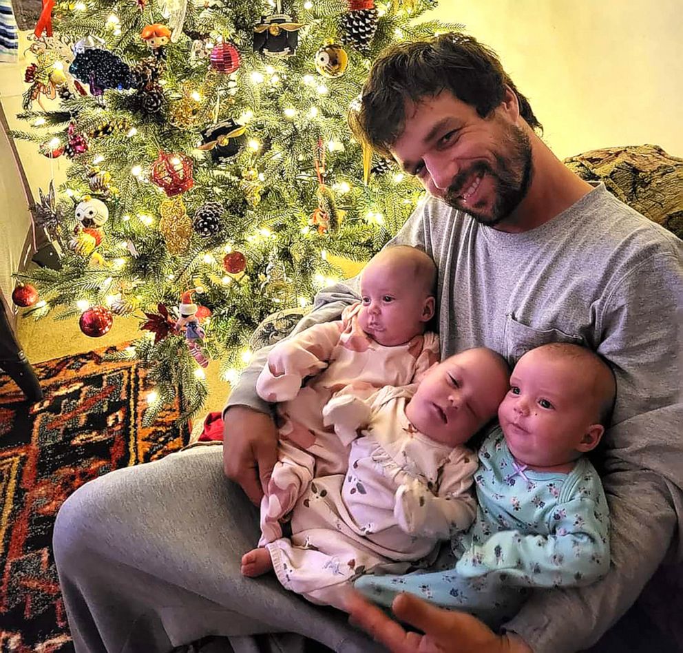 PHOTO: Derrick Stroud smiles for a photo while holding his triplet daughters, including Amelia, next to a Christmas tree.