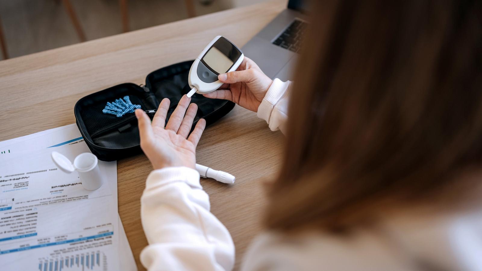 PHOTO: A girl sits at a table, using a glucometer to measure her blood sugar.