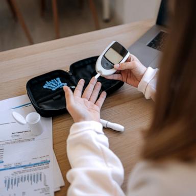 PHOTO: A girl sits at a table, using a glucometer to measure her blood sugar.