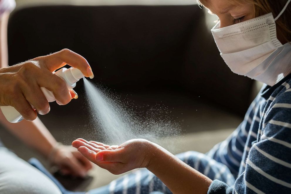PHOTO: Unrecognizable single parent spraying hand sanitizer to her little boy's hand. Boy is with face mask.