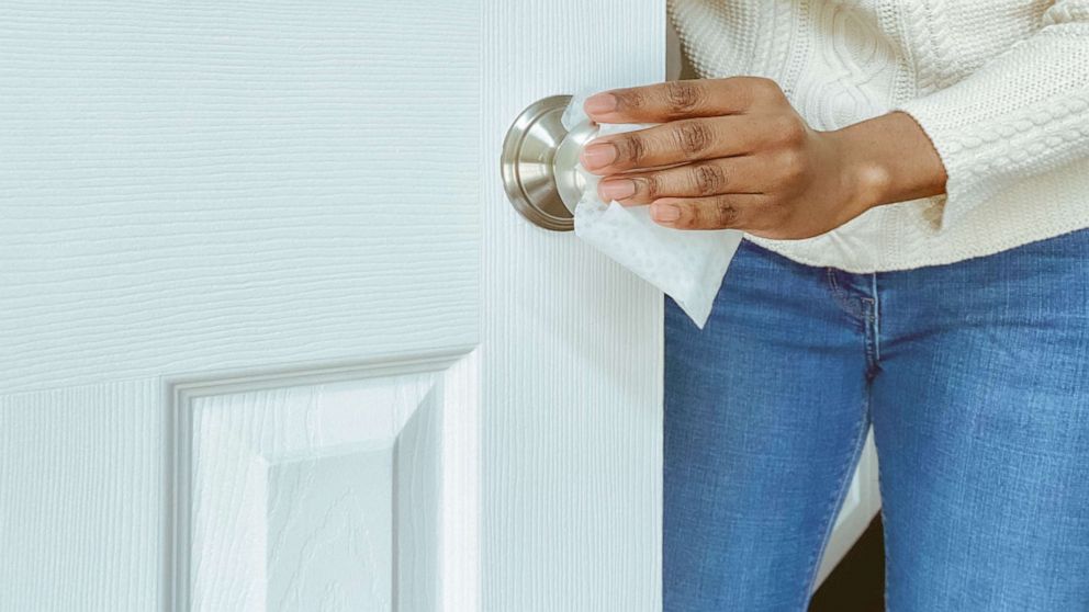 PHOTO: A woman cleans a doorknob on interior door with disinfectant wipe