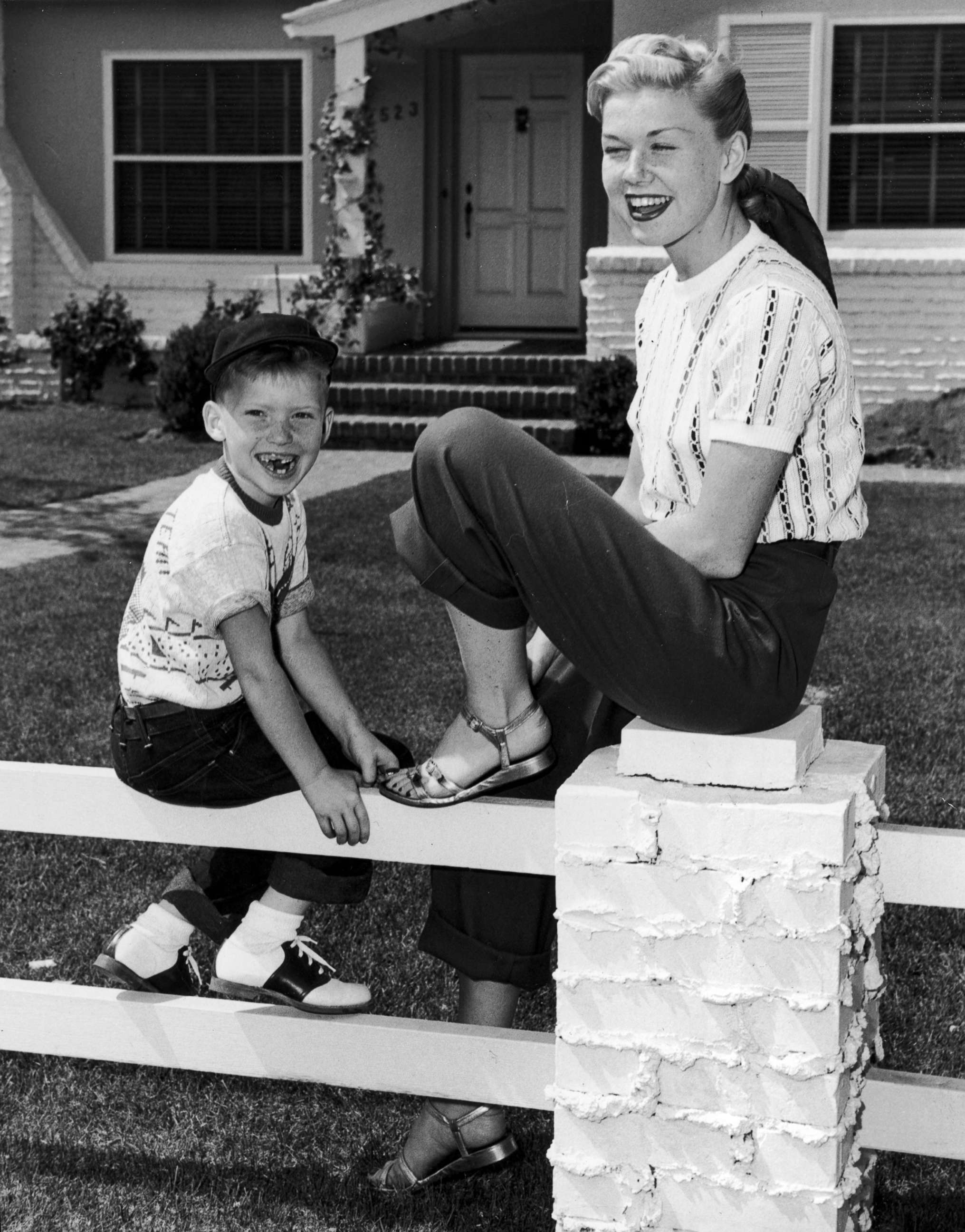 PHOTO: American actress and singer Doris Day sits on a fence in front of a house with her son, Terry.