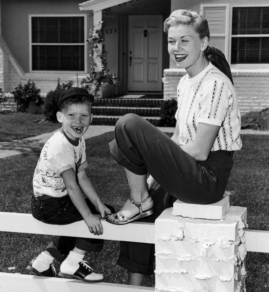 PHOTO: American actress and singer Doris Day sits on a fence in front of a house with her son, Terry.