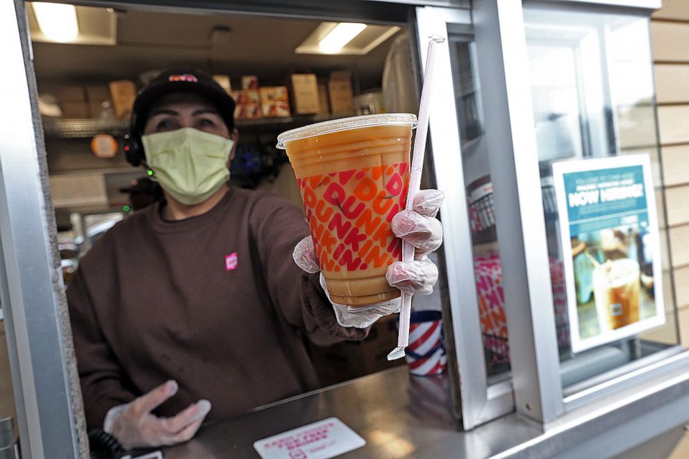 PHOTO: A Dunkin' worker hands a coffee out of a drive-thru window wearing gloves and a mask as the Coronavirus continues to spread on March 17, 2020 in Norwell, Massachusetts.