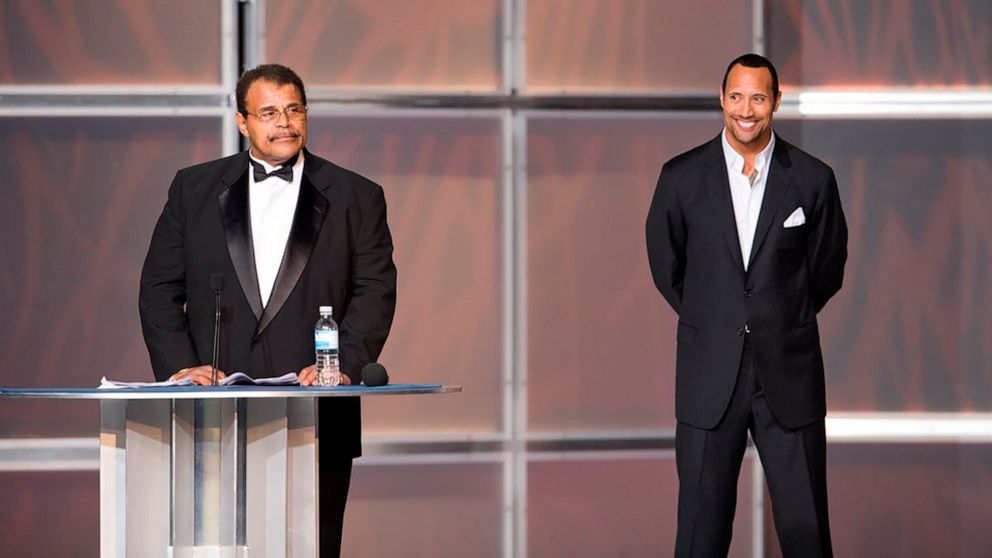 PHOTO: In this 2008 photo provided by WWE, Inc., Rocky "Soul Man" Johnson, left, speaks at his WWE Hall of Fame induction ceremony, as his son, Dwayne âThe Rockâ Johnson watches. Rocky Johnson died Wednesday, Jan. 15, 2020. He was 75.
