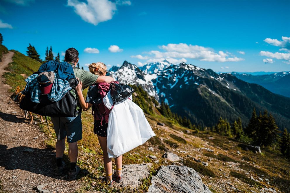 PHOTO: A bride and groom hike with their wedding gown and tux on the way to their adventure elopement.