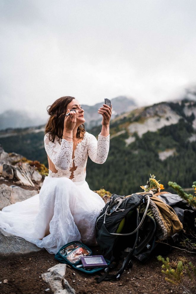 PHOTO: A bride touches up her makeup on a mountaintop during an adventure elopement.