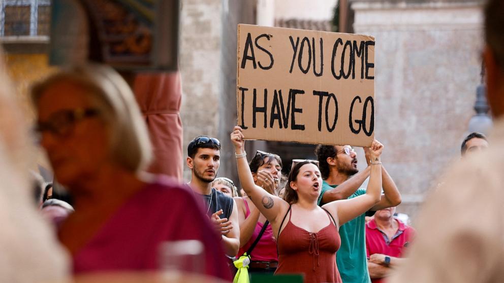 PHOTO: A woman raises a placard in front of tourists seated at a bar, in Palma de Mallorca, Spain, June 15, 2025.