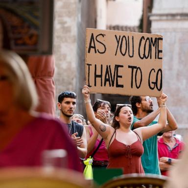 PHOTO: A woman raises a placard in front of tourists seated at a bar, in Palma de Mallorca, Spain, June 15, 2025.