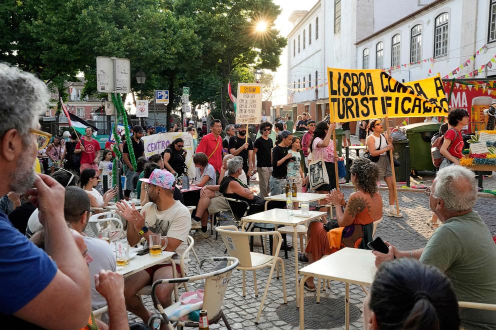 PHOTO: Tourists at a bat terrace watch, and some applaud, as demonstrators carrying a banner with the words "Lisbon against touristification" stage a protest against mass tourism in Lisbon, June 15, 2025.