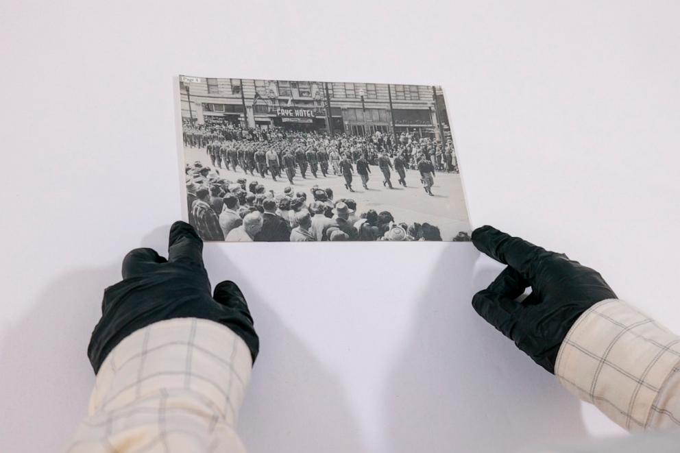 PHOTO: Caitlin Oiye Coon holds a photo from Densho’s collection, likely showing a military parade of the U.S. Army’s 442nd Regimental Combat Team, a segregated unit that comprised Japanese American soldiers.