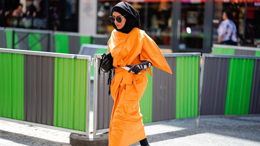 A guest wears an orange dress, black gloves with printed words, a burka, outside Alexis Mabille, during Paris Fashion Week, July 3, 2018 in Paris.