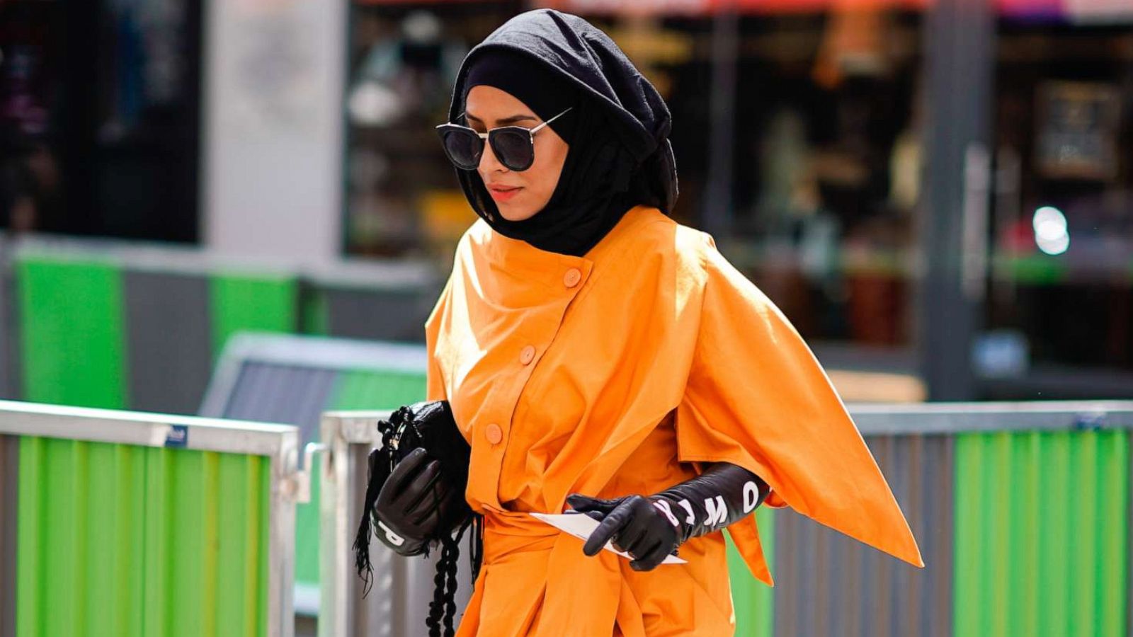 PHOTO: A guest wears an orange dress, black gloves with printed words, a burka, outside Alexis Mabille, during Paris Fashion Week, July 3, 2018 in Paris.