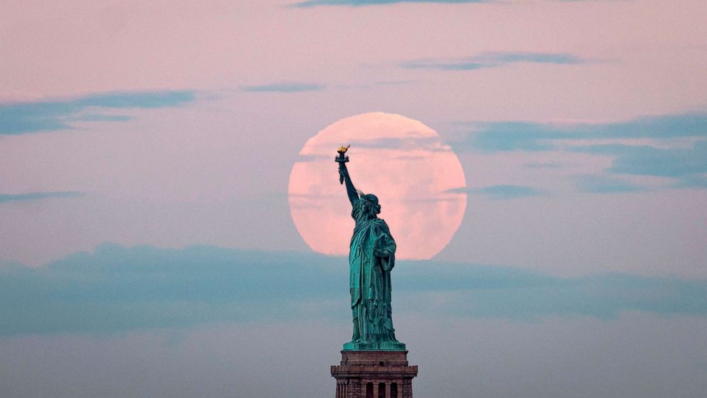 PHOTO: May's full Moon, known as the Full Flower Moon and is the last supermoon of the year, sets behind the Statue of Liberty on May 7, 2020 in New York City. 