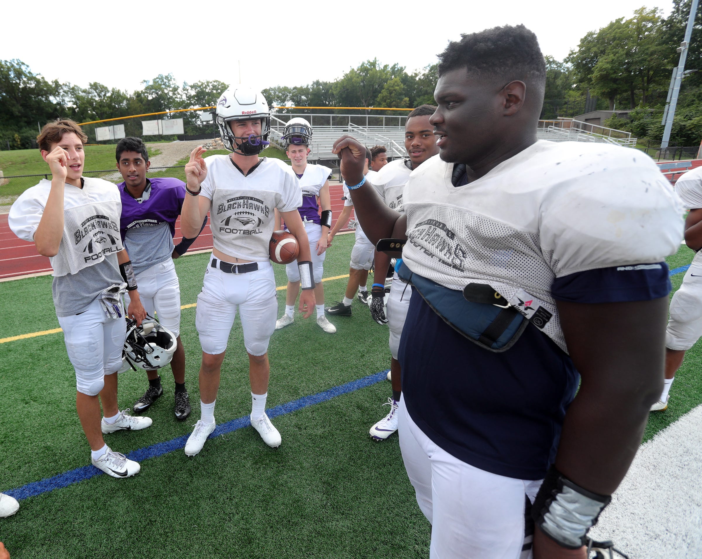 PHOTO: Bloomfield Hills' Dean Bolton, Santhosh Ramachandran and Tasnner Slazinski sign with Bloomfield Hills defensive lineman Devin Holmes, right, who is deaf, during practice on Wednesday, Sept. 4, 2019, at Bloomfield Hills High School.